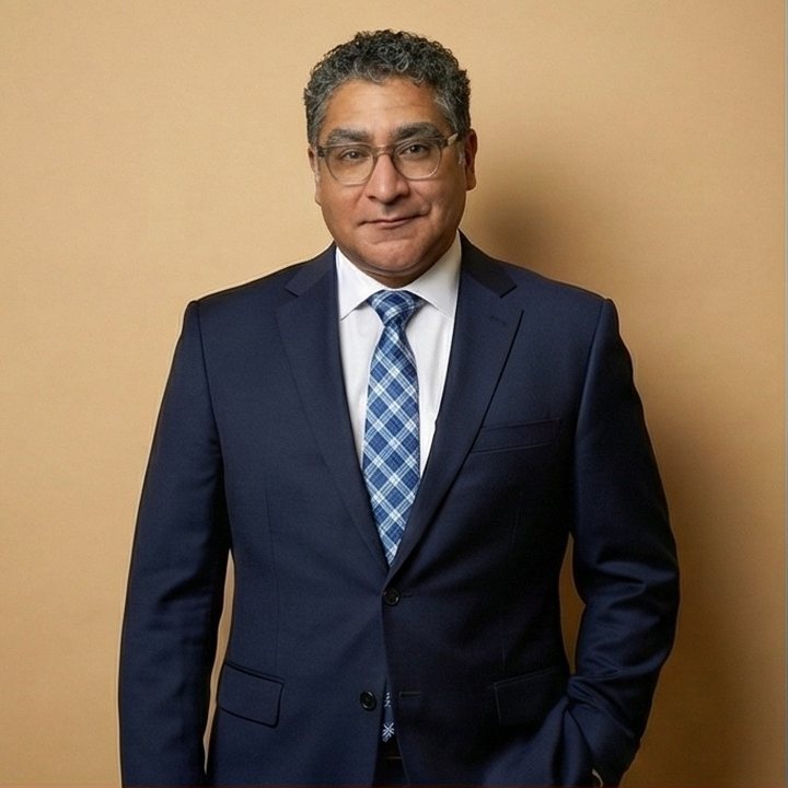 David Vega in a navy suit and blue tie against a tan background